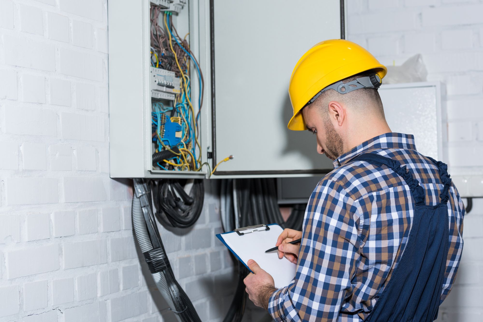 Electrician reviewing failed electrical inspection deficiencies beside an electrical panel